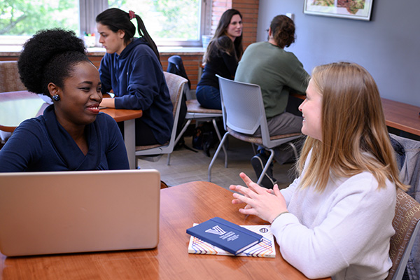 Two student sit together at a table with a laptop open in front of them.