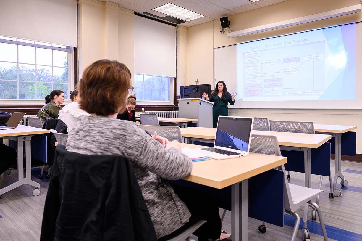 A student presents to a class with a presentation on a screen behind her.