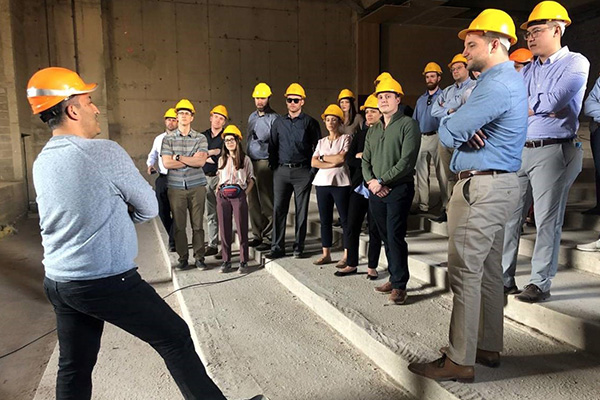 Students stand together at a work site with hard hats on.
